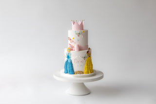 Two-tiered cake with princess theme on a white stand against a light gray background