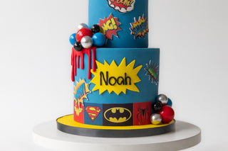 Colorful superhero-themed birthday cake with 'Noah' on a white background